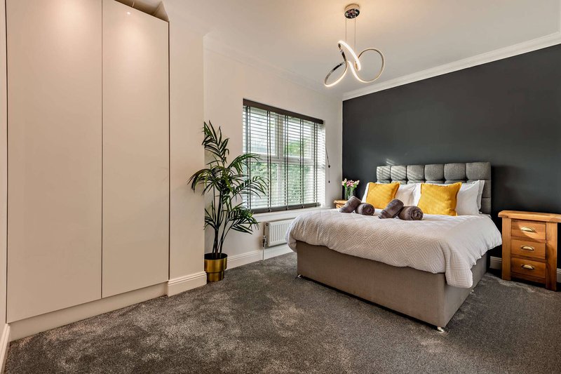 Modern bedroom with grey upholstered bed, black accent wall, wooden nightstand and potted plant