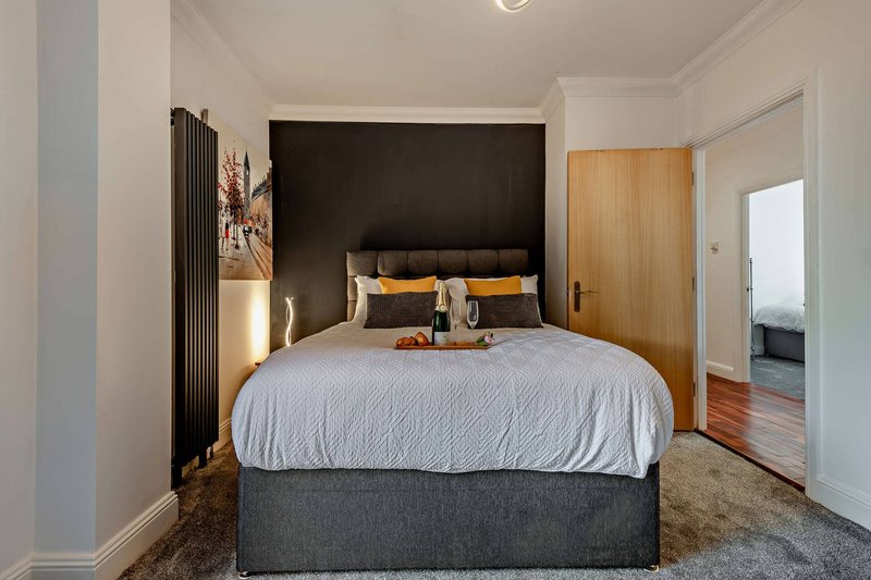 Modern bedroom with double bed, black headboard, grey bedding, and wooden wardrobe
