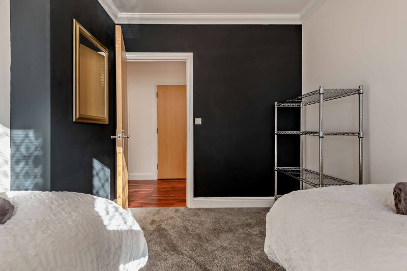 Bedroom with two beds, dark accent wall, wooden door and metal shelving unit