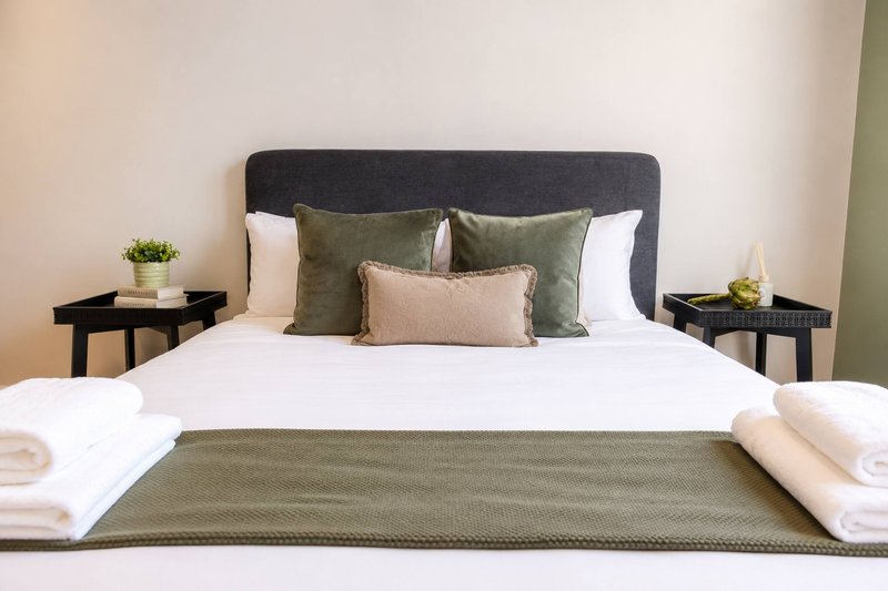 Bedroom with dark headboard, white bedding, green cushions and throws, bedside tables