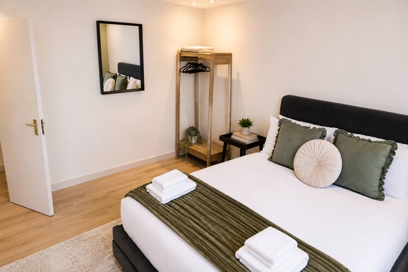 Bedroom with double bed, green cushions, wooden mirror, clothing rack and warm lighting