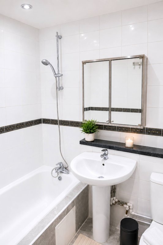 Modern bathroom with white tile walls, pedestal sink, mirror, bathtub and shower fixture