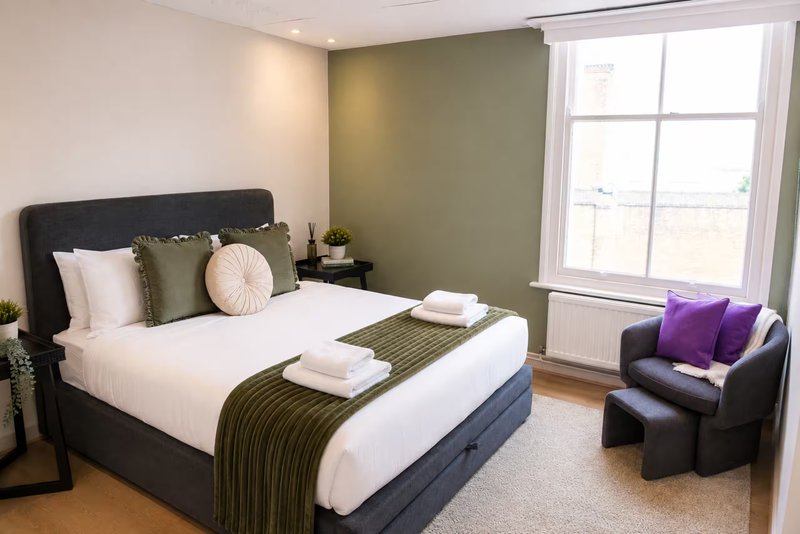 Modern bedroom with black bed, olive accent wall, armchair, and large window overlooking landscape