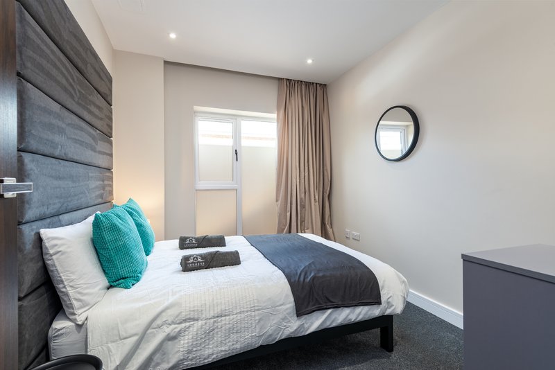 Modern bedroom with single bed, teal throw pillow, dark headboard and wall clock
