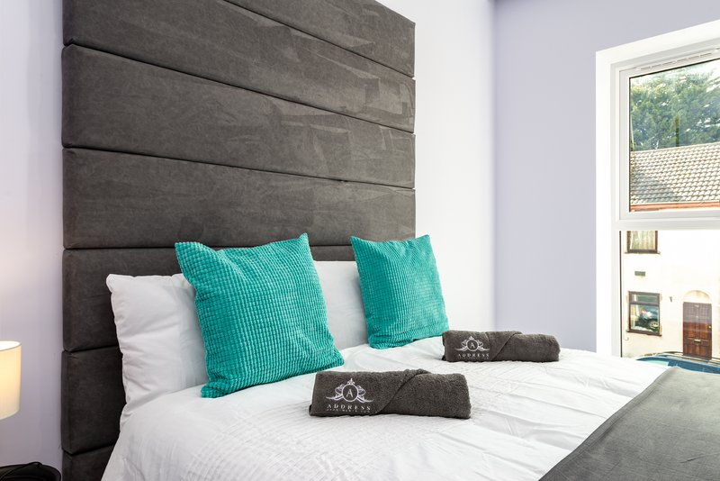 Modern bedroom with grey padded headboard, turquoise cushions, white bedding and window view
