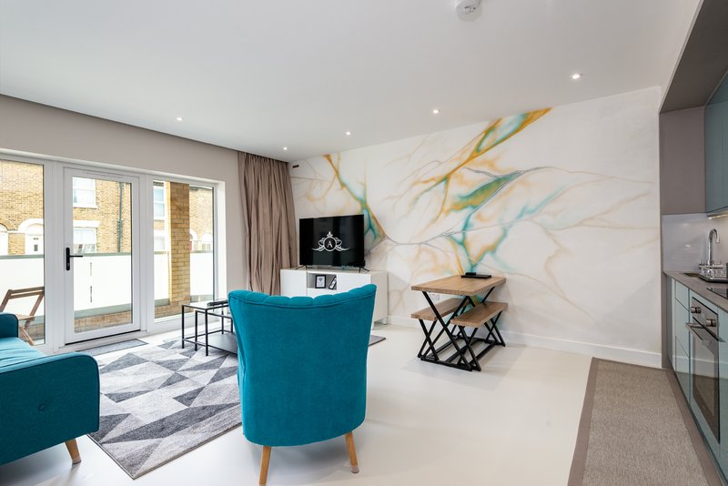 Modern open-plan living space with turquoise armchair, marble accent wall, kitchen area and glass doors