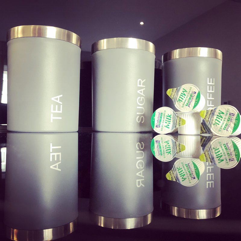 Three branded kitchen canisters with tea, sugar, and coffee labels, and packaged items on shelf