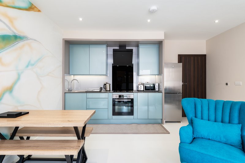 Modern open-plan kitchen and dining area with blue cabinetry, wooden table, and bright blue armchair