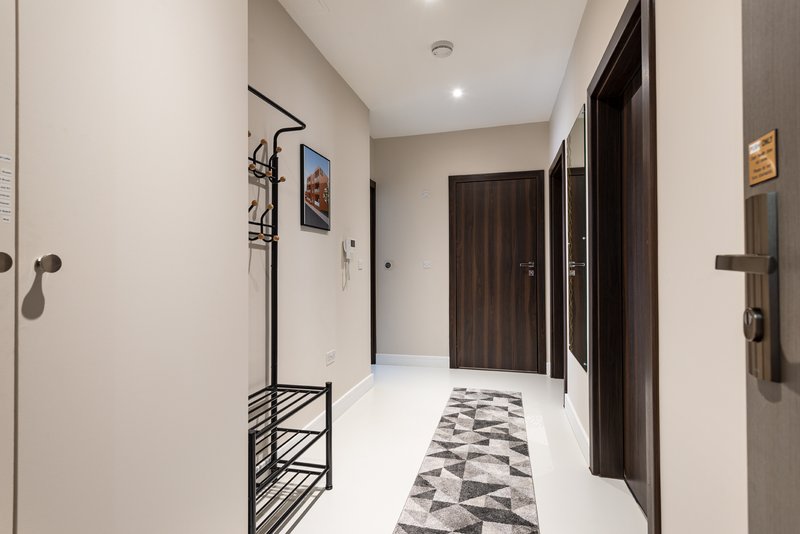 Modern hallway with white walls, dark wooden doors, geometric floor runner and wall-mounted coat rack