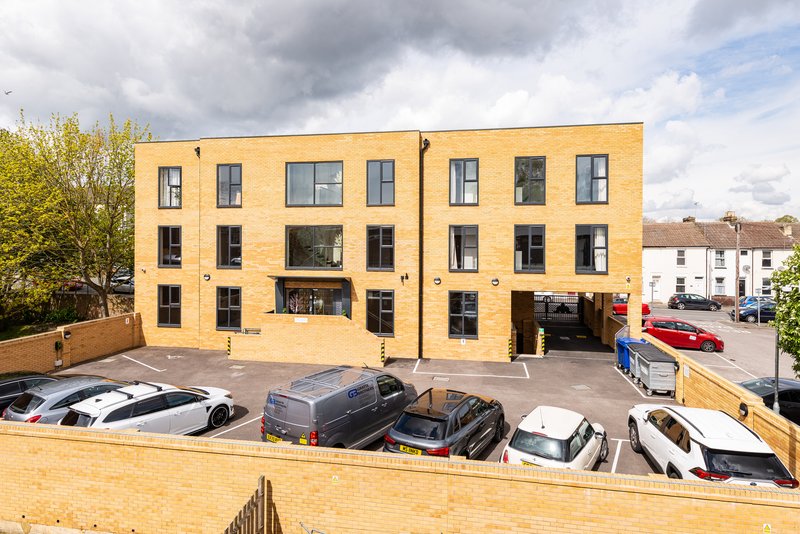 Modern yellow-brick apartment building with parked cars in front courtyard