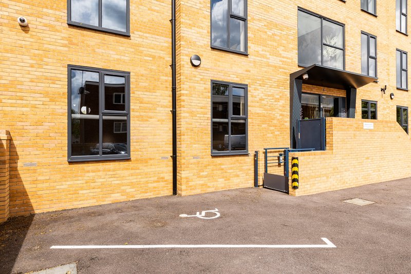 Modern brick building exterior with windows, entrance door, and marked parking spaces