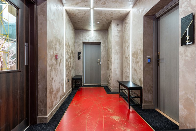 Modern hallway with red epoxy flooring, textured walls, wooden door and elevator doors