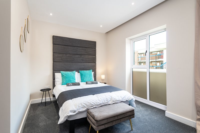 Modern bedroom with dark headboard, double bed, turquoise pillows, and glass balcony doors