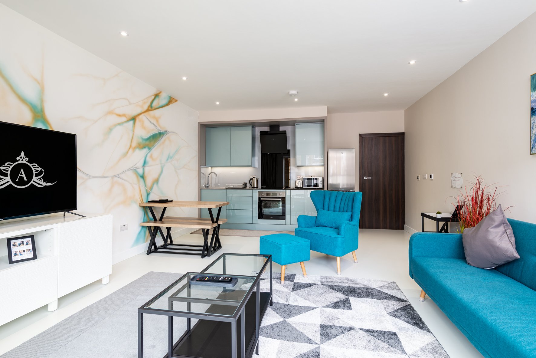 Open-plan living area with blue sofa, dining table, kitchen, and wall art