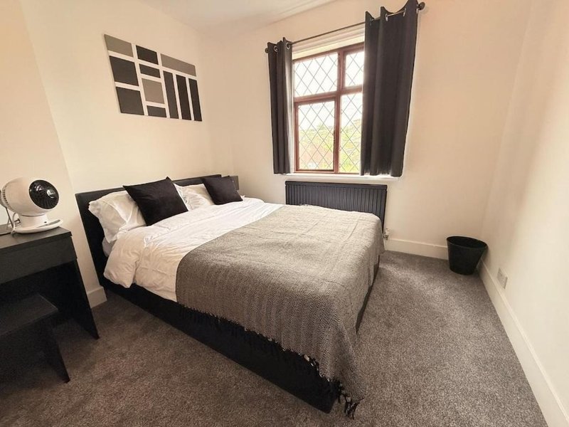 Bedroom with double bed, black frame, grey carpet, window with dark curtains