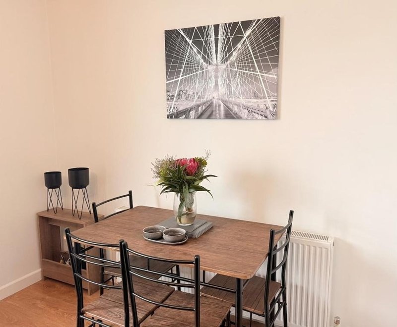 Dining area with wooden table, black chairs, fresh flowers in vase, and wall art