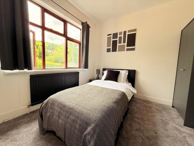 Bedroom with single bed, window with red frame, radiator and grey carpet flooring
