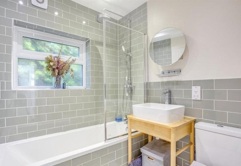 Modern bathroom with green subway tile, white bathtub, wooden vanity and round mirror