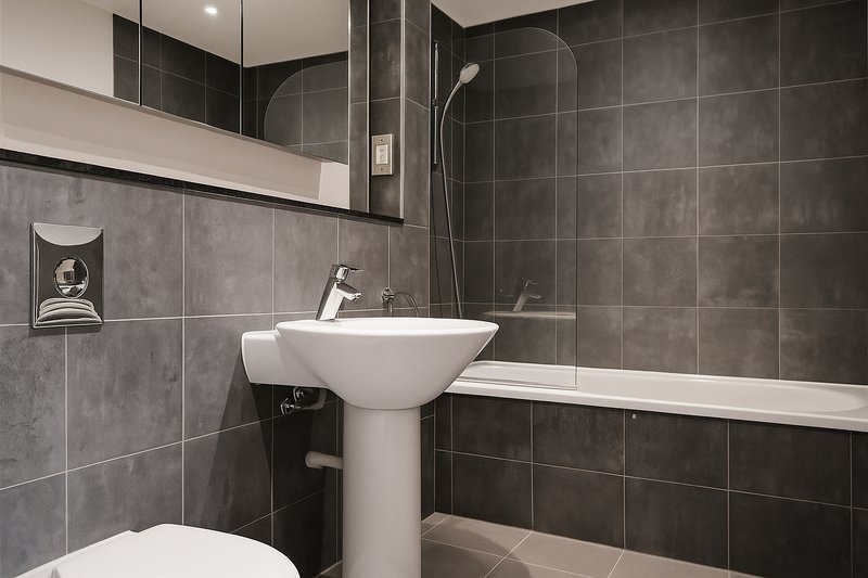 Modern bathroom with pedestal sink, grey tile walls, mirror and shower enclosure