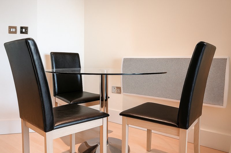Minimalist dining area with glass table, black leather chairs and grey acoustic panel