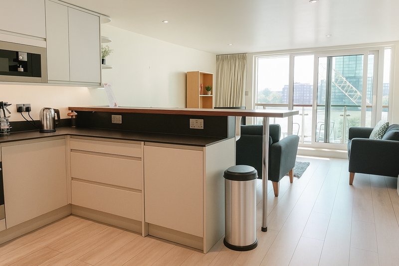 Open-plan kitchen and living area with beige cabinetry, black countertop, stainless steel appliances, and city views from large windows