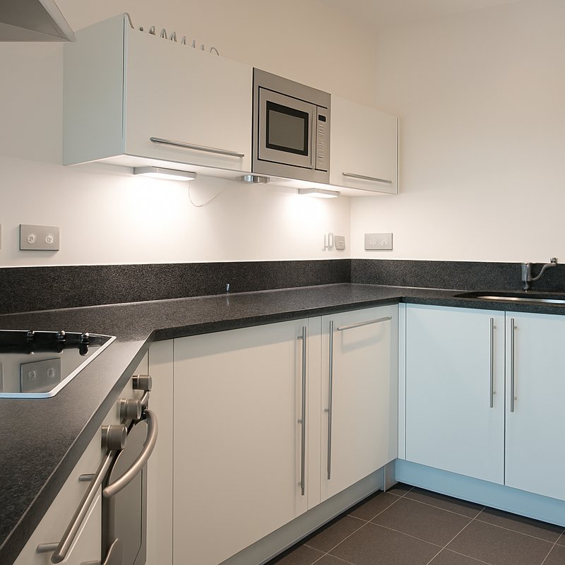 Modern kitchen with white cabinetry, black granite countertop, stainless steel appliances and under-cabinet lighting