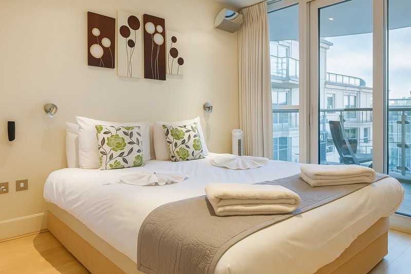 Modern bedroom with double bed, decorative wall art, large windows overlooking city buildings