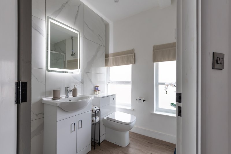Modern bathroom with white vanity, illuminated mirror, toilet and window with blinds