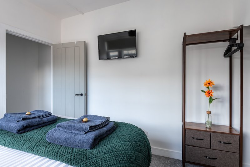 Bedroom with double bed, folded towels, wall-mounted TV, wardrobe and flower vase