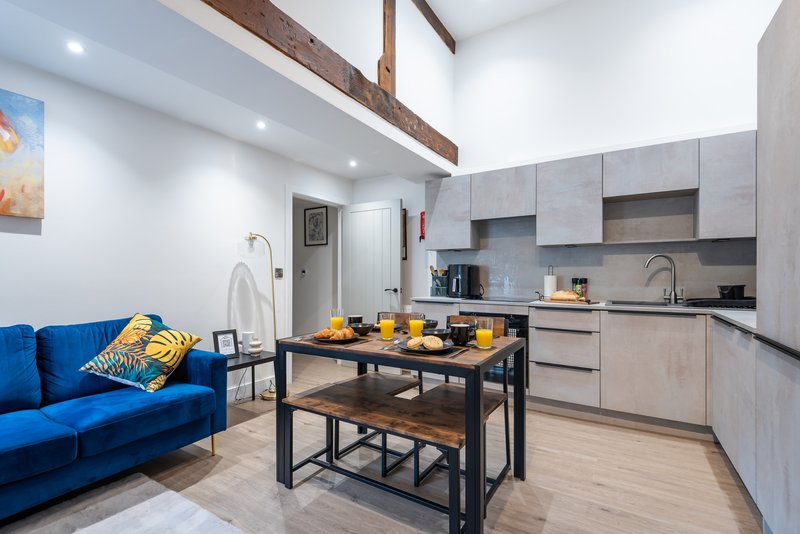 Open-plan kitchen and living area with blue sofa, wooden beams, and dining island