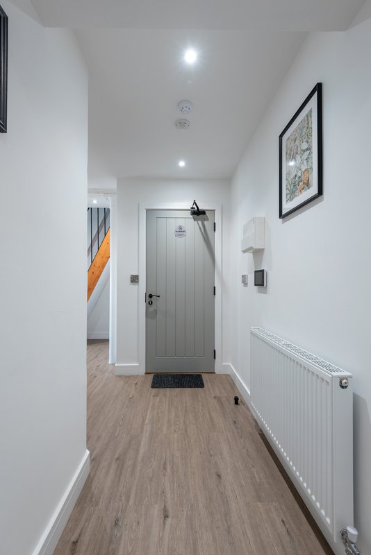 Modern hallway with wooden flooring, white walls, gray door and wall-mounted radiator