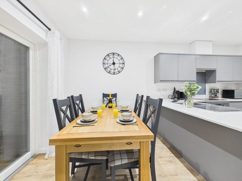 Modern kitchen-diner with wooden table, black chairs, grey cabinetry and wall clock