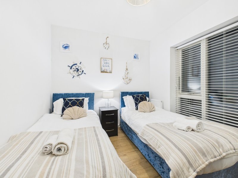 Twin bedroom with striped bedding, blue headboards, nautical wall decor and louvered window blinds