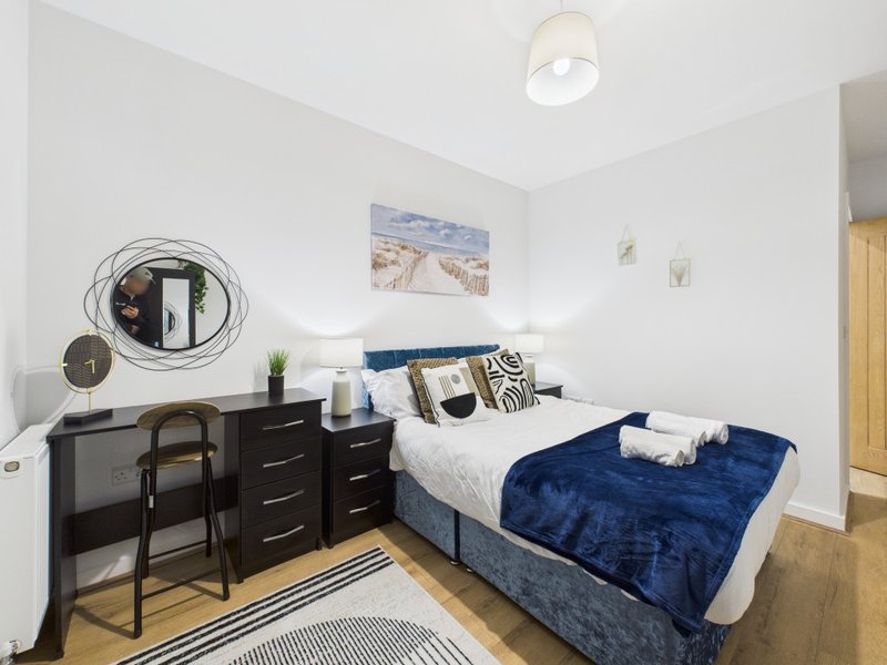 Modern bedroom with double bed, navy bedding, desk, chair and wooden flooring
