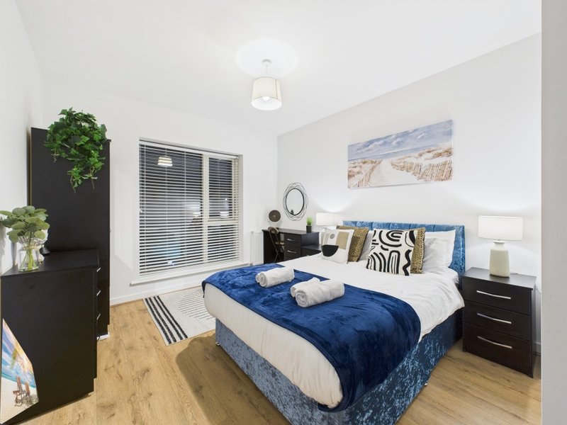 Modern bedroom with double bed, blue bedding, black furniture, wooden floor and window blinds