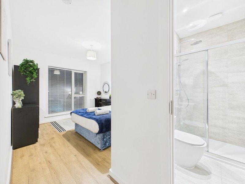 Modern bedroom with double bed, wooden flooring, and ensuite bathroom with shower enclosure