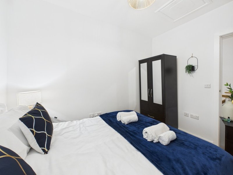 Modern bedroom with double bed, navy and white bedding, black wardrobe and hanging plant