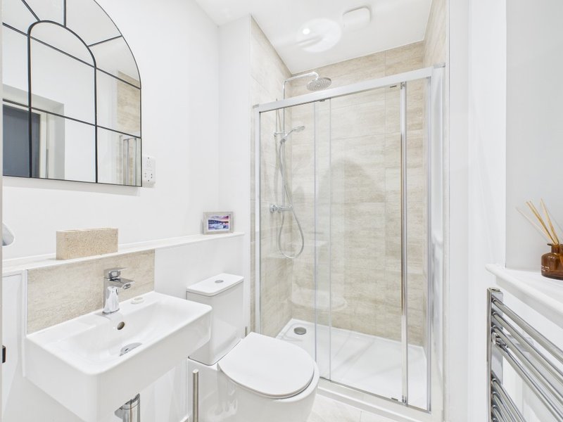 Modern bathroom with dual sink vanity, toilet, and enclosed shower enclosure with stone tile