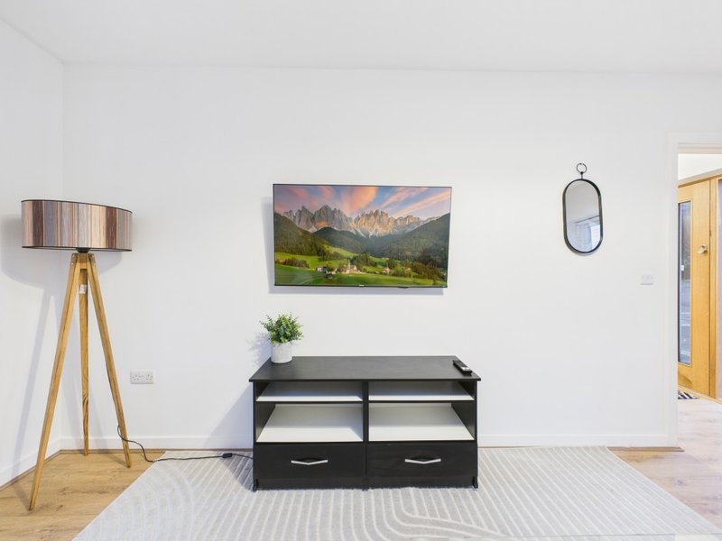 Modern living room with black storage unit, tripod floor lamp, landscape artwork and mirror