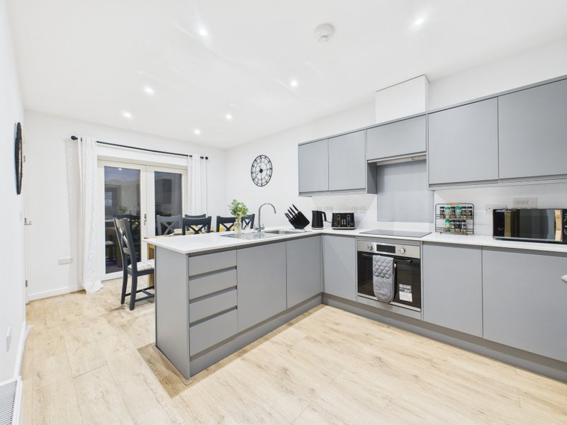 Modern kitchen with gray cabinetry, white countertops, island seating, and wood-effect flooring