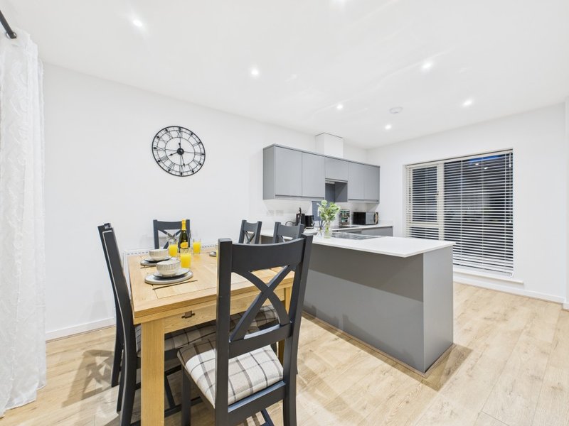 Modern open-plan kitchen and dining area with wooden table, black chairs, and grey cabinetry