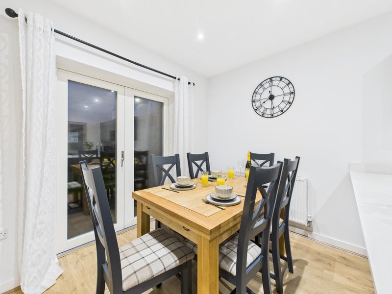Dining room with wooden table, black chairs, clock on wall, and glass doors to patio