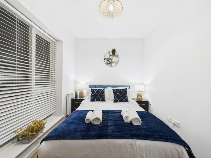 Modern bedroom with blue velvet bedding, white pillows, dark headboard and pendant lighting