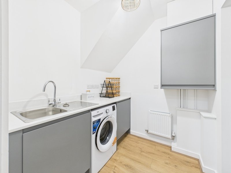 Modern laundry room with washing machine, sink, wooden flooring and roller blind