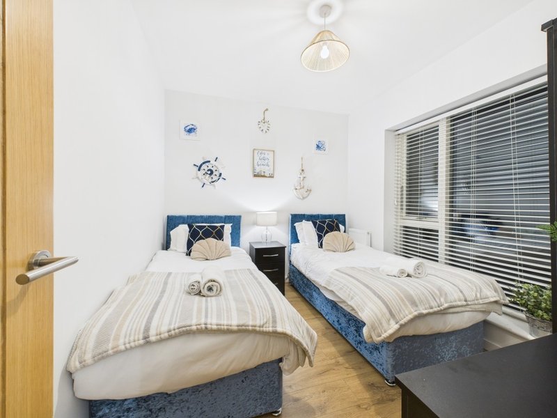 Bright bedroom with two single beds, blue headboards, striped bedding, wooden flooring and venetian blinds