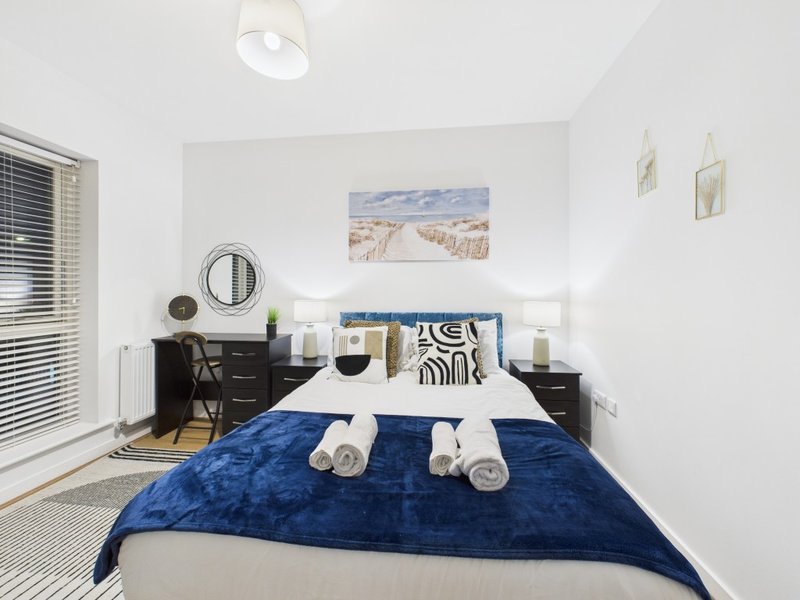 Bright bedroom with double bed, blue velvet throw, black bedside tables, desk, and minimalist wall art