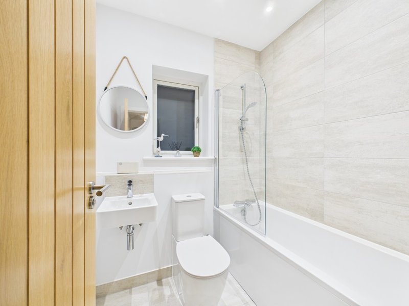 Modern bathroom with white sink, toilet, bathtub, round mirror and wooden wall paneling