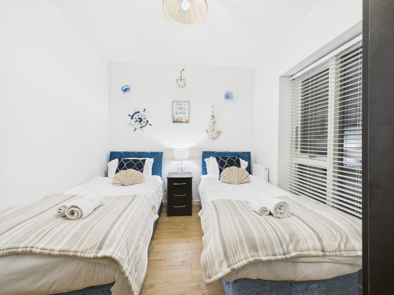 Twin bedroom with striped bedding, blue pillows, wooden floor and nautical wall decor