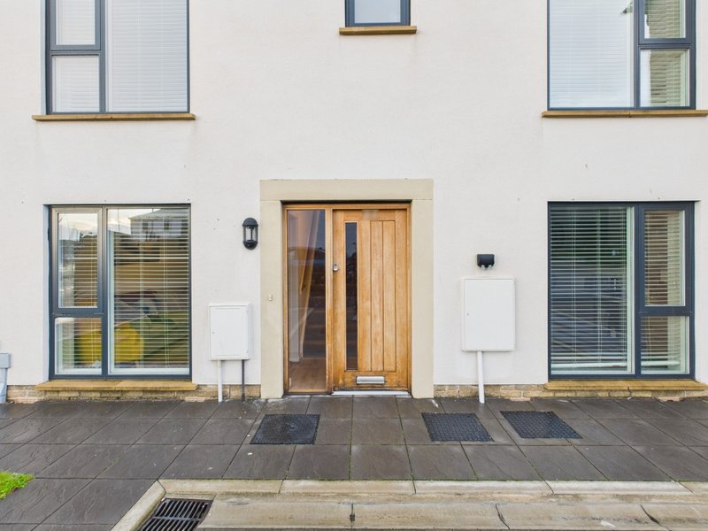 Modern white building exterior with wooden door, multiple windows, and paved courtyard area