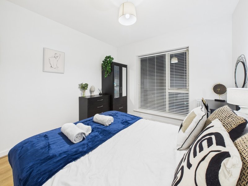 Modern bedroom with double bed, blue throw, white towels, black furniture and sliding wardrobe doors